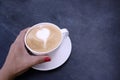 Woman hand holding latte coffee with white milk foam in heart shape on black background table Royalty Free Stock Photo