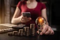 Woman hand holding lightbulb with coins stack on desk. Royalty Free Stock Photo