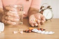 Woman hand holding medicines in hand with glass of water and clock on desk