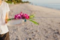 Woman hand holding orchid flowers and bottle of water on the beach. Royalty Free Stock Photo