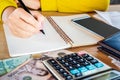 Woman hand holding pen writing on notebook with money, calculator and smart phone on desk Royalty Free Stock Photo