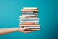 Woman hand holding pile of books, teal background. Education or knowledge concept Royalty Free Stock Photo