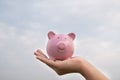 Woman hand holding Pink piggy bank on sky background, step up growing business to success and saving for retirement  concept Royalty Free Stock Photo