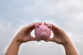 Woman hand holding Pink piggy bank on sky background, step up growing business to success and saving for retirement  concept Royalty Free Stock Photo