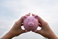 Woman hand holding Pink piggy bank on sky background, step up growing business to success and saving for retirement  concept Royalty Free Stock Photo