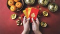 Woman hand holding pow or red packet, orange and gold ingots on a red background