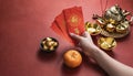 Woman hand holding pow or red packet, orange and gold ingots on a red background