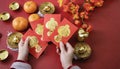 Woman hand holding pow or red packet, orange and gold ingots on a red background