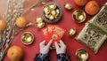 Woman hand holding pow or red packet, orange and gold ingots on a red background