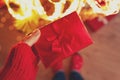 Woman hand holding red Christmas gift box wrapped red ribbon against background of Christmas tree lights. Christmas or New Year