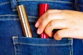 Woman hand holding a red and golden lipsticks inside of jeans back pocket