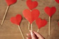 Woman hand holding red paper heart. Many hearts on a wooden background in defocus. Valentine`s Day concept