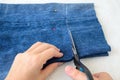 Woman hand holding a scissors and cutting blue denim shorts to make them shorter. Making jeans shorts. On a white