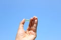 Woman hand holding single yellow Cod Liver Oil capsule on blue sky background Royalty Free Stock Photo