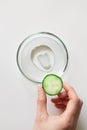 Woman hand holding slice of cucumber in hand and transparent cosmetic gel smudge in glass petri dish on white background Royalty Free Stock Photo