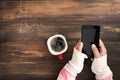 Woman hand holding smart phone with hot cup of coffee on wood table