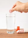 Woman hand holding soluble effervescent vitamin pill over a glass of pure drinking water. Vitamins and nutritional supplements.