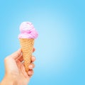 Woman hand holding wafer cone with pink  ice cream on blue background Royalty Free Stock Photo