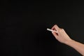 Woman hand holding white chalk in front of blank school blackboard