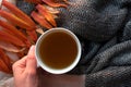 Woman hand holding white cup with herbal hot tea with copy space. Knitted scarf and orange autumn leaves, top view. Drink Royalty Free Stock Photo