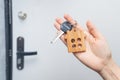 Woman hand holds key to the apartment with a wooden house keychain in the background of the entrance door to the flat. The Royalty Free Stock Photo