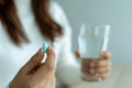 The woman hand holds a pill and a glass of water. The patient is about to take the medicine. Taking care of the sick body using an