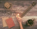 Woman hand lights a incense stick from a Buddha holder on a vintage natural wooden surface with books, twine and incense