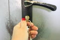 Woman hand locking or unlocking door with key on bunch on grey old metal shabby door background