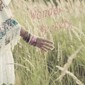 Woman hand with lot of boho style braceletes touching grass , summer day in the field with quote wonder seekers