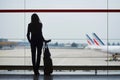 Woman with hand luggage in international airport, looking through the window at planes