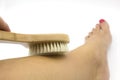 Woman hand makes legs massage with wooden soft massage brush for body and legs on white background. Anti cellulite home spa Royalty Free Stock Photo