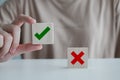 Woman hand pick correct check mark on wooden cube with cross symbol stand on table.