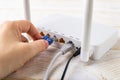 Woman hand plugging a blue network cable into socket of a white Wi-Fi wireless router on a white wooden table. Wlan router with Royalty Free Stock Photo