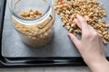 Woman hand poured granola in glass jar on parchment paper on baking sheet, close-up. Made homemade breakfast