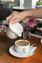 Woman hand is pouring milk in coffee cup Royalty Free Stock Photo