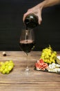 Woman hand pouring Red wine in glass from bottle, brie cheese, blue cheese, grapes, jamon meat, salami on black slate Royalty Free Stock Photo