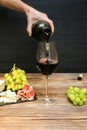 Woman hand pouring Red wine in glass from bottle, brie cheese, blue cheese, grapes, jamon meat, salami on black slate Royalty Free Stock Photo