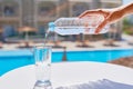 Woman hand pouring water in a glass from plastic bottle agains swimming pool background Royalty Free Stock Photo