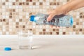 Woman hand pours pure drinking water from a blue plastic bottle into a glass on a white wood table. Quench thirst and health care Royalty Free Stock Photo