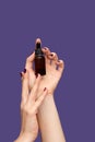 Female hand holding essential oil bottle on purple background. Female hand with glitter purple manicure. Essential parfume bottle Royalty Free Stock Photo