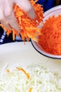 Woman hand put fresh grated carrot to the metal bowl with chopped cabbage Royalty Free Stock Photo