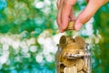 Woman hand put gold coin money in the glass jar on table in garden with green background, for saving banking finance concept. Royalty Free Stock Photo