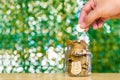 Woman hand put gold coin money in the glass jar on table in garden with green background, for saving banking finance concept. Royalty Free Stock Photo