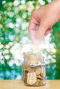 Woman hand put gold coin money in the glass jar on table in garden with green background, for saving banking finance concept. Royalty Free Stock Photo