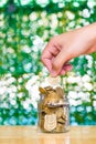 Woman hand put gold coin money in the glass jar on table in garden with green background, for saving banking finance concept. Royalty Free Stock Photo