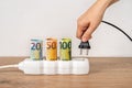 Woman hand putting electric plug into power strip with rolled euro currency banknotes. Soaring of electricity prices in Europe.