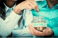 Woman hand putting money coin in the glass jar labeled SAVINGS