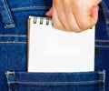 Woman hand putting a white small notebook inside of jeans back pocket