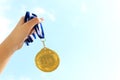 Woman hand raised, holding gold medal against sky. award and victory concept Royalty Free Stock Photo