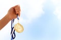 Woman hand raised, holding gold medal against sky. award and victory concept Royalty Free Stock Photo